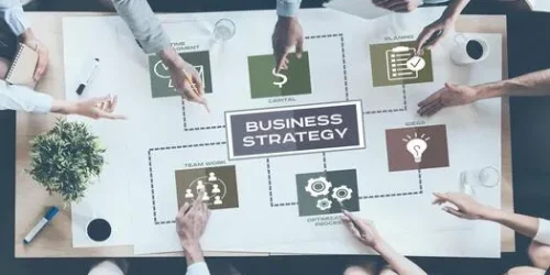 discussing-company-strategy-top-view-of-business-people-pointing-large-paper-with-conceptual-business-icons-while-sitting-together-at-the-desk-photo